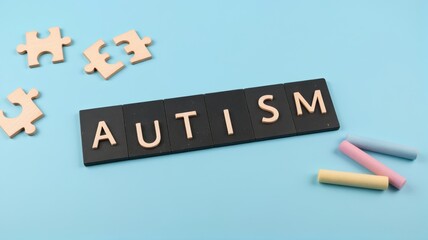 The word 'AUTISM' spelled out with tiles on a blue background alongside puzzle pieces and colorful chalks.