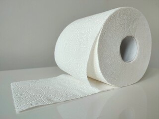 White toilet paper roll on a clean surface, unrolling slightly, highlighting its textured pattern and practical household use
