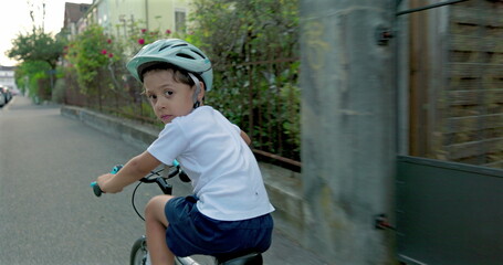 Obraz premium Young boy cycling down a residential street, wearing a helmet for safety, enjoying an active ride while exploring his neighborhood on a sunny day, reflecting childhood freedom and health