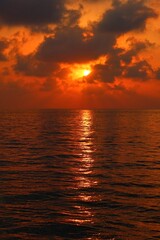 Romantic morning by the sea. Vivid rising red sun, calm morning water surface under the dark clouds. Distant dark sky, water and colorful sunrise. Morning by the ocean, travel landscape photography. 