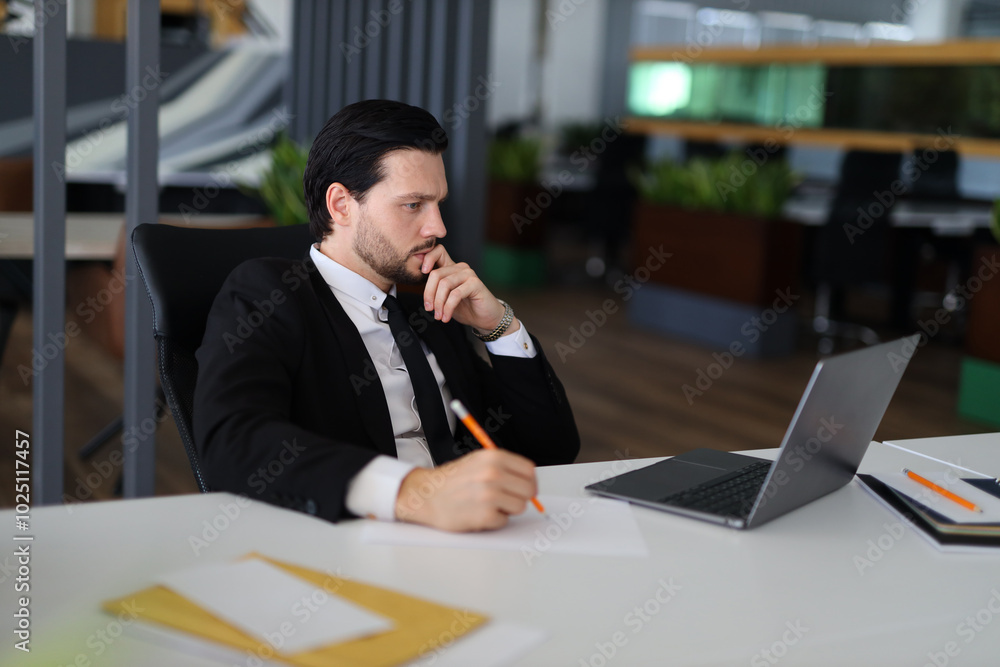 Aufkleber a man in a suit is sitting at a desk with a laptop and a pencil. he is writing something on a piece 