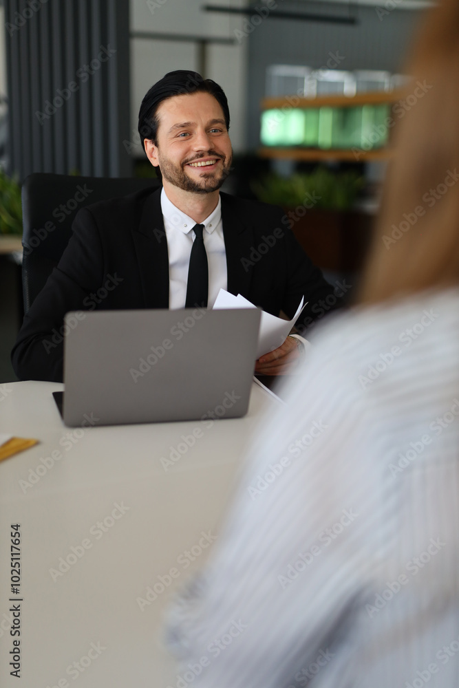 Poster a man in a suit is sitting at a desk with a laptop and a piece of paper. he is smiling and he is in 
