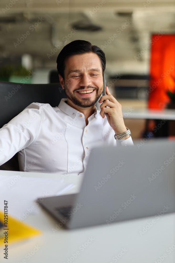 Poster a man is talking on his cell phone while sitting at a desk. he is smiling and he is enjoying the con