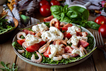 Salad with shrimp, tomatoes, arugula, cheese in a plate on a wooden background. Delicious salad with shrimp and vegetables for breakfast. close-up