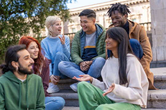Diverse students socializing outdoors, multicultural group using smartphones on campus steps