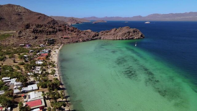 Aerial drone footage of a clear water bay with coral reef surrounded by desert and rocky cliffs on a clear summer day