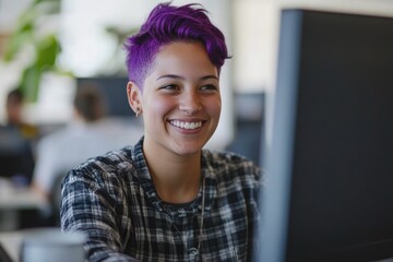 A woman with vibrant purple hair sits in front of a computer, smiling
