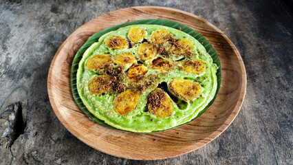 Vibrant green banana pancake with caramelized banana slices and brown sugar, served on a wooden plate with a rustic dark wood background