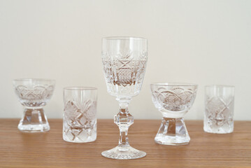 Different types of small elegant empty crystal glasses on the brown wooden table. Close-up. Copy space. Selective focus.