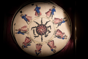 Intricate circular artwork featuring colorful figures dancing around a spiral design in a historical exhibit setting