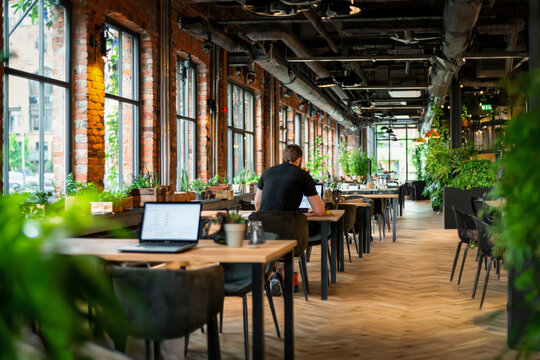 An Entrepreneur Working In A Modern Co-Working Space, Using A Laptop And Smart Devices To Connect With Clients Globally, Illustrating The Integration Of Technology In Business