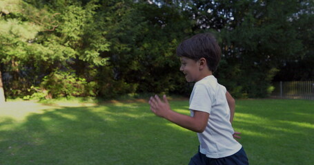 Young boy running in a park, wearing a white shirt, with a determined expression, surrounded by greenery, enjoying an energetic moment outdoors on a sunny day