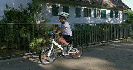Fototapeta premium Young boy riding his bike along a riverbank, wearing a helmet for safety, urban and natural scenery, enjoying a sunny day, engaging in an active outdoor lifestyle