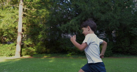 Young boy running in a park, wearing a white shirt, with a determined expression, surrounded by...