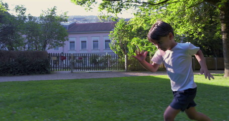 Young boy sprinting across a grassy park, with a determined expression, surrounded by trees and...