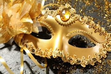 Beautiful golden carnival mask and confetti on gray textured table, top view