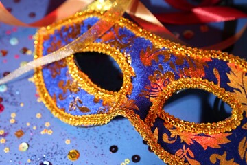 Beautiful carnival mask, ribbons and confetti on blue background, closeup
