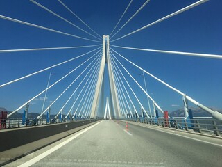 Fototapeta premium Photo of the iconic Charilaos Trikoupis Bridge connecting Rio with Antirio, Peloponnese to the mainland, Greece. Beautiful white suspension bridge against the blue sky.
