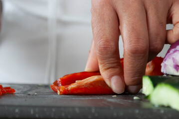 Close-up of a woman's hands cutting vegetables with a knife on a cutting board. Home cooking concept, gastronomy, veganism.
