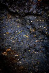 Dark textured stone surface with golden flecks. The stone is cracked, adding a sense of natural ruggedness and strength.