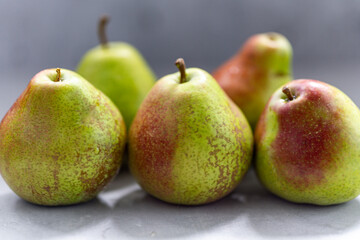 Ripe pears with reddish spots on a light surface. A few fruits are blurred in the background.