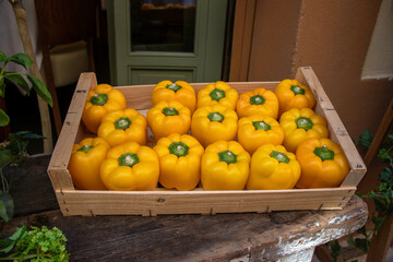 A vegetable crate box of yellow peppers all standing upright in a rustic setting