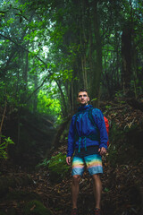 Male tourist in hard shell rain jacket looks down a misty jungle trail in the rain. Poco dos Pulgas Waterfalls, Madeira Island, Portugal, Europe.