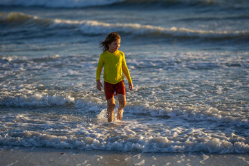 Exited carefree little boy running on wet coast near waving sea on sunny summer day. Child running at summer beach. Carefree child. Excited child running in the summer sea. Cute kid run on summer sea.