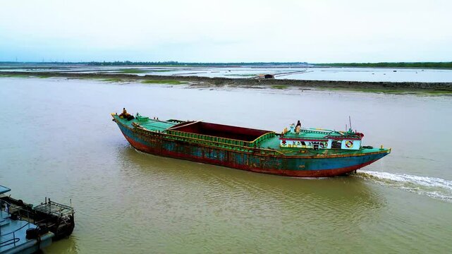 Top view of an empty green bulkhead ship moving forward through the water. The vessel's green color contrasts with the dark sea, as it cuts through the waves, heading steadily toward its destination