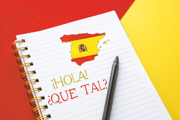 notebook with the spanish flag and the inscription Hello, How are you in Spanish, learning concept