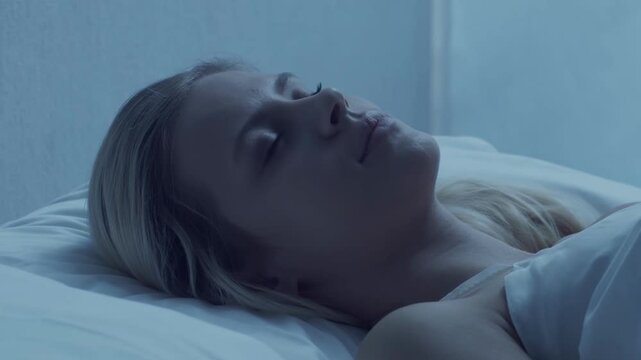 Young woman lying in the bed at night and having insomnia disease. Beautiful blond sleeping girl. Twilight in the bedroom, moonlight from the window. Sleeplessness, health and rest concept.