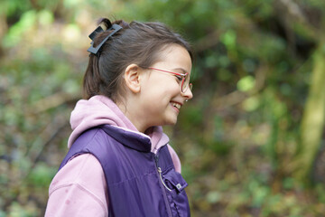 Little beautiful girl with glasses in a hoodie and vest against the background of a dark autumn...