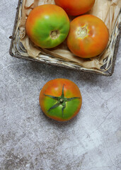 Vertical shot, group of tomatoes on wicker tray base on gray stone base, copy space and overhead view.