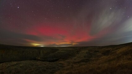 4K Timelapse. Vivid aurora borealis captured in motion with clouds in the dead of night on October 10, 2024. River, tree and rocks in the foreground. Big red glow at the moment of maximum storm