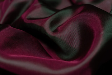 A close-up of soft, flowing synthetic fabric with an iridescent finish that shifts from deep...