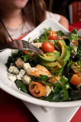 Spinach salad served with grilled chicken, ripe avocado slices, blue cheese crumbles, cherry tomatoes, and a variety of fresh greens. The dish looks healthy and appetizing, ideal for a wholesome and n