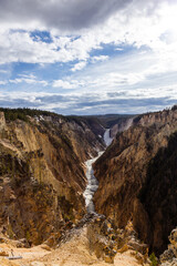 Majestic View of the Grand Canyon of the Yellowstone in Wyoming, USA with Towering Waterfalls and Rugged Cliffs Under a Dramatic Cloudy Sky