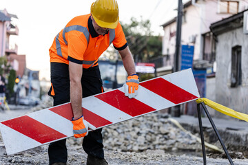 Construction worker lifting a barrier on a road under repair in an urban area during daylight hours