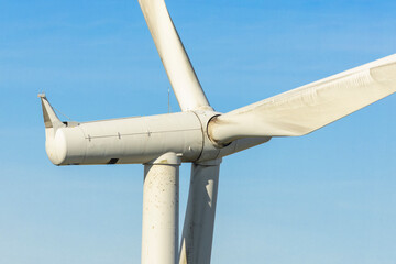 Close-up of large wind turbine nacelle hub and blades against clear blue sky at renewable energy...