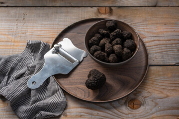 bowl with black truffles and truffle slicer on wooden table