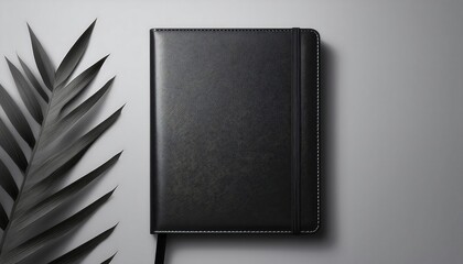 Top-down view of a black leather notebook mockup on a light grey background with a leaf accent. Generative AI