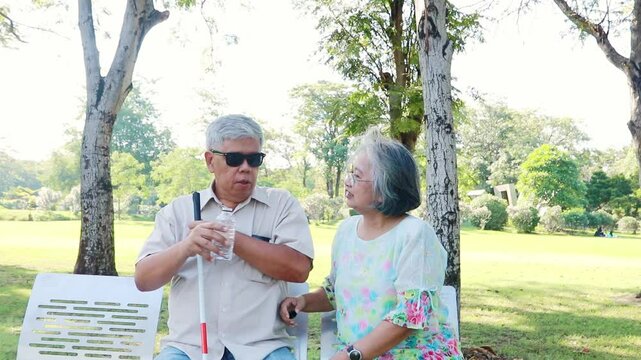 Elderly couple with blind husband drinking water fresh to quench their thirst on a hot day in the garden while their wife sits by their side, looking after them warmly and happily.