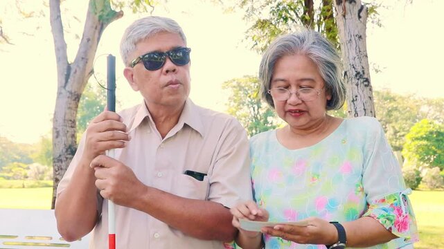Wife takes care of her blind husband and tells stories from photos to her blind husband, who can hear the words and memories of the people in the photos together happily in a park.