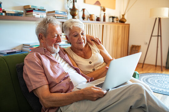 Happy senior couple using laptop together on a couch at home