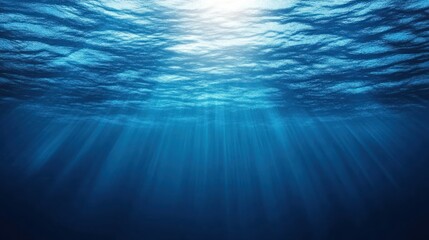 Sunbeams pierce through the deep blue ocean water, creating a mesmerizing underwater scene.