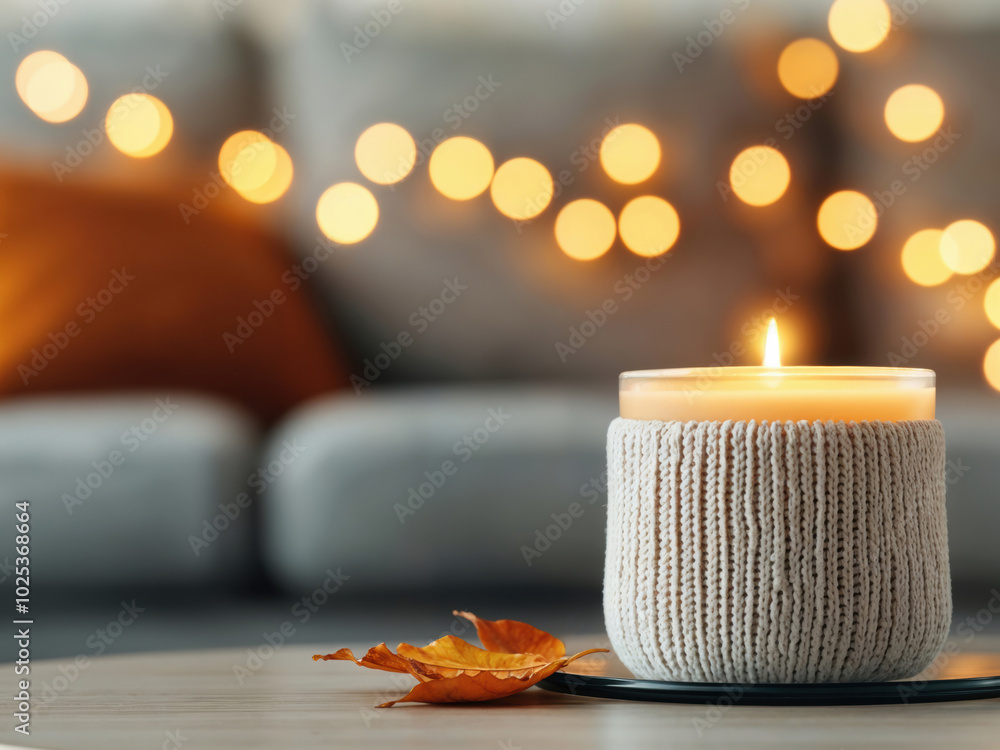 Poster lit candle in a knitted holder with autumn leaf and bokeh lights in the background. cozy fall decor 