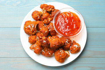 Tasty cauliflower buffalo wings and sauce on light blue wooden table, top view