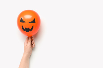 Female hand with funny Halloween orange balloon on white background