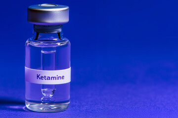 Single ketamine vial on a blue background with space for text overlay