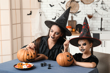 Little girl with her mother painting Halloween pumpkins in kitchen